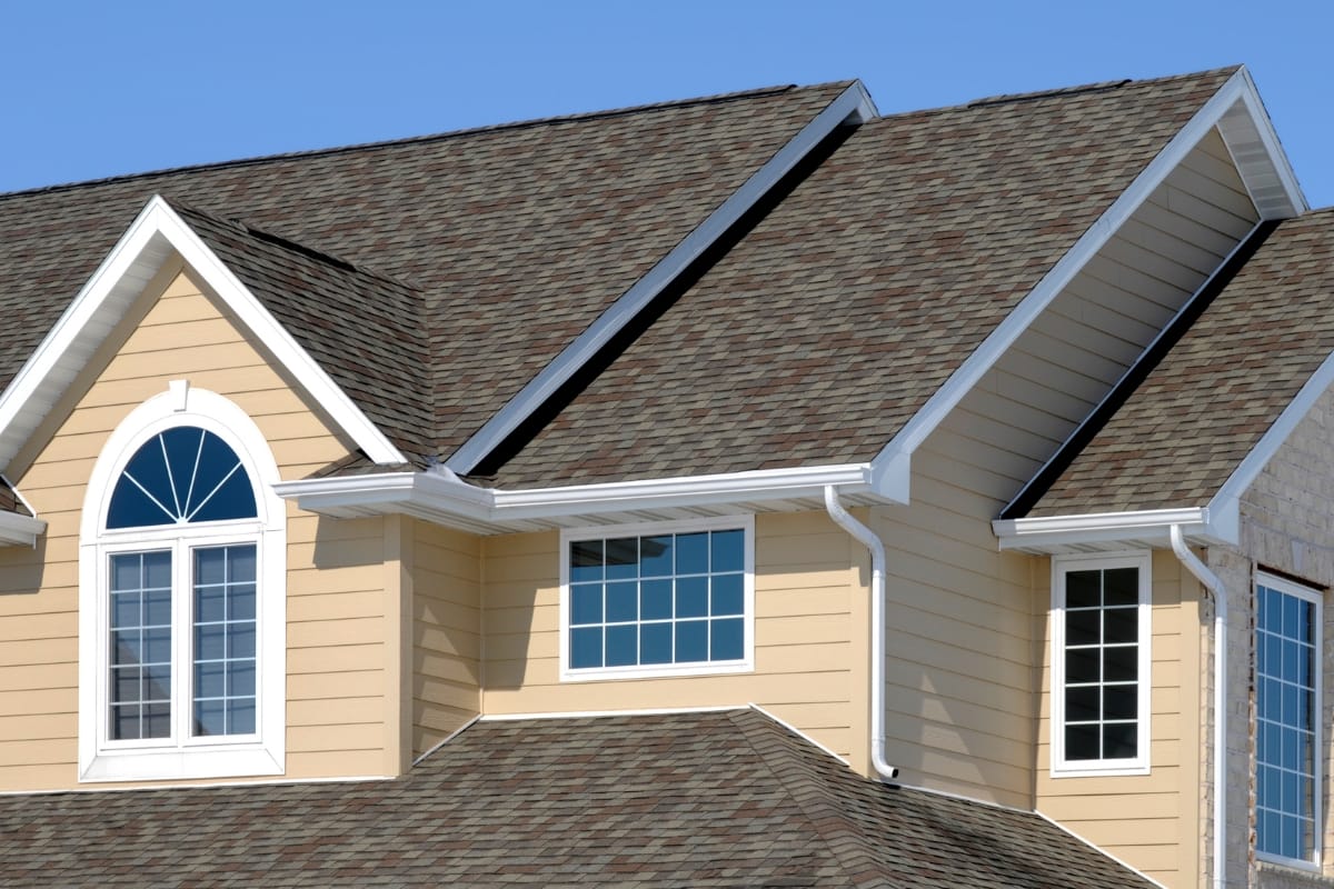 A modern house with yellow siding and multiple roof gables, featuring white-framed windows and a prominent arched window, showcases the meticulous work of residential contractors.