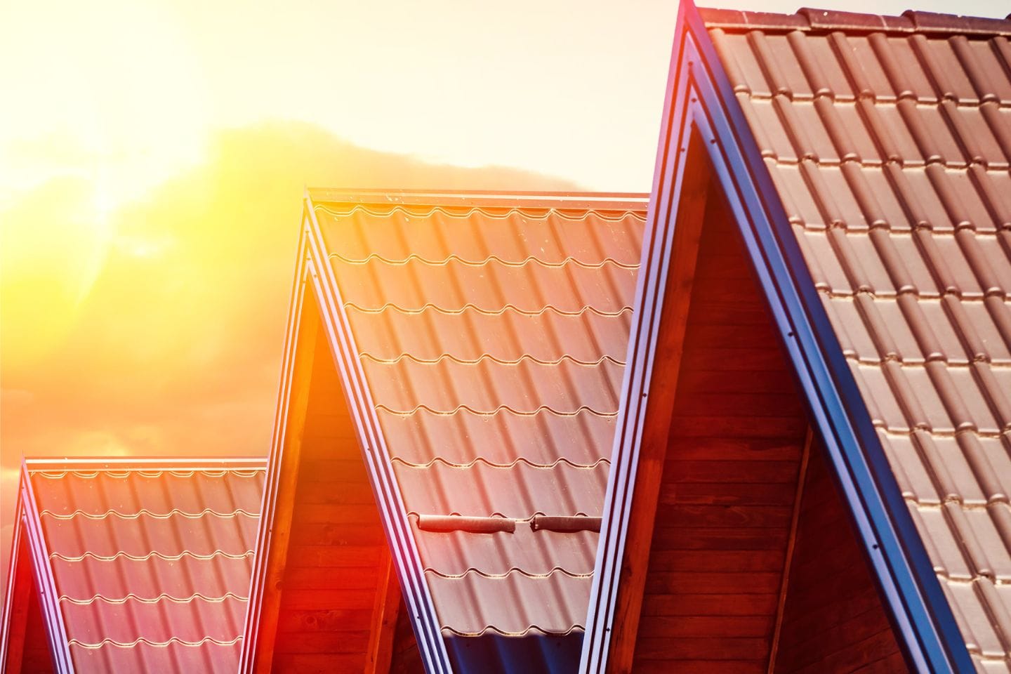 Close-up of multiple gable roofs with red tile shingles, illuminated by warm sunlight from the left side of the image—showcasing a stunning property.