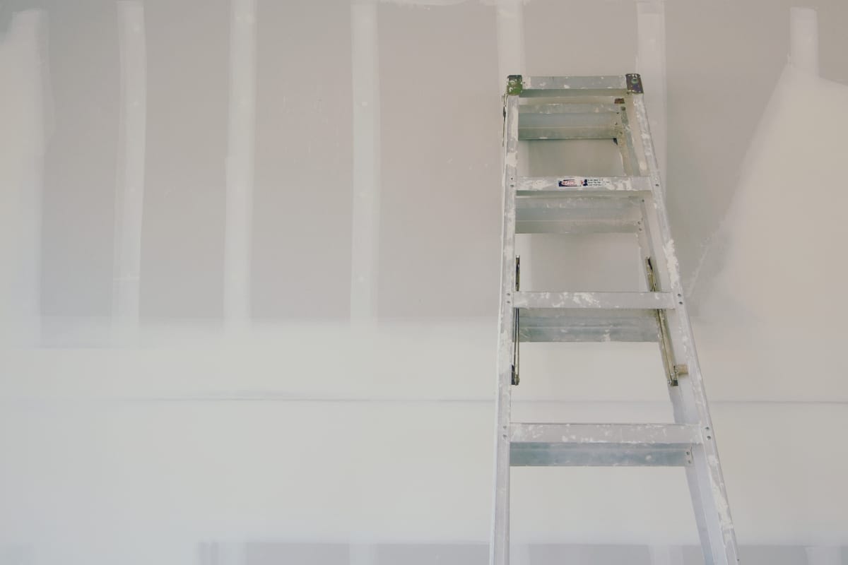 A metal ladder leans against an unfinished drywall surface, showcasing visible seams and patches, ready for professional services to transform the space.