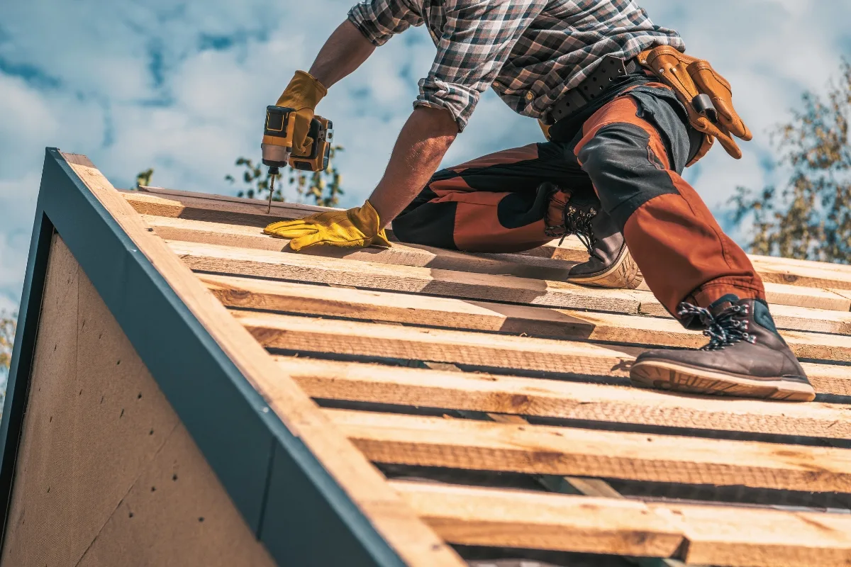 A dedicated worker in professional attire skillfully handles a power tool to install wooden boards on a roof, set against the backdrop of a partly cloudy sky. I'm sorry, but the description you provided is incomplete; additional context would be helpful for identifying relevant SEO keywords.