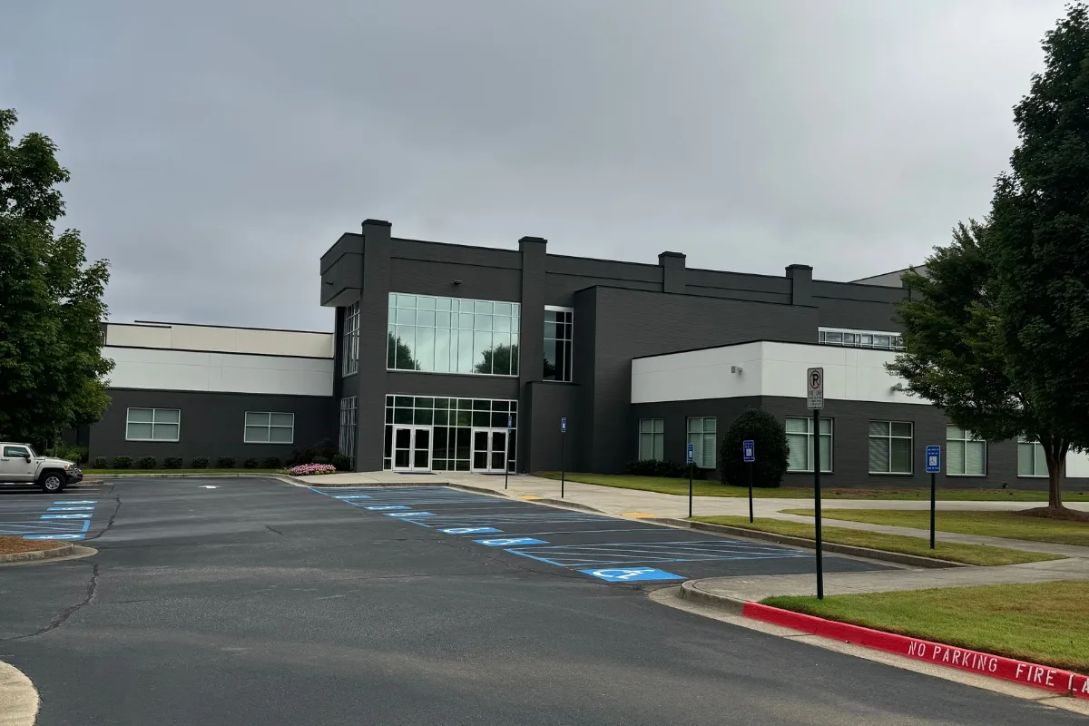 A modern, dark-gray commercial building with large windows stands amidst a cluster of trees under a cloudy sky, offering accessible parking in front. With the current description provided, I apologize for any lack of specific SEO keywords.