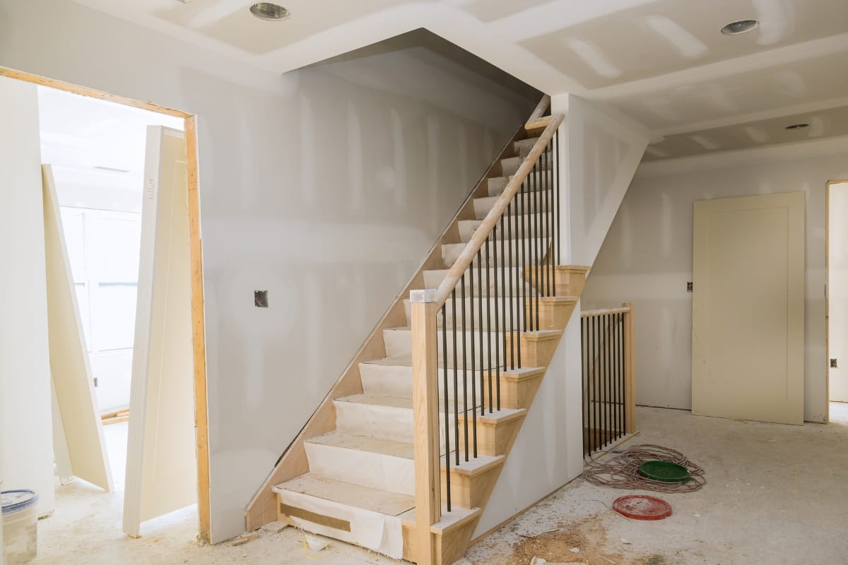 Partially constructed interior staircase with unfinished walls and railing, showcasing ongoing construction services; materials scattered on the floor indicate active progress.