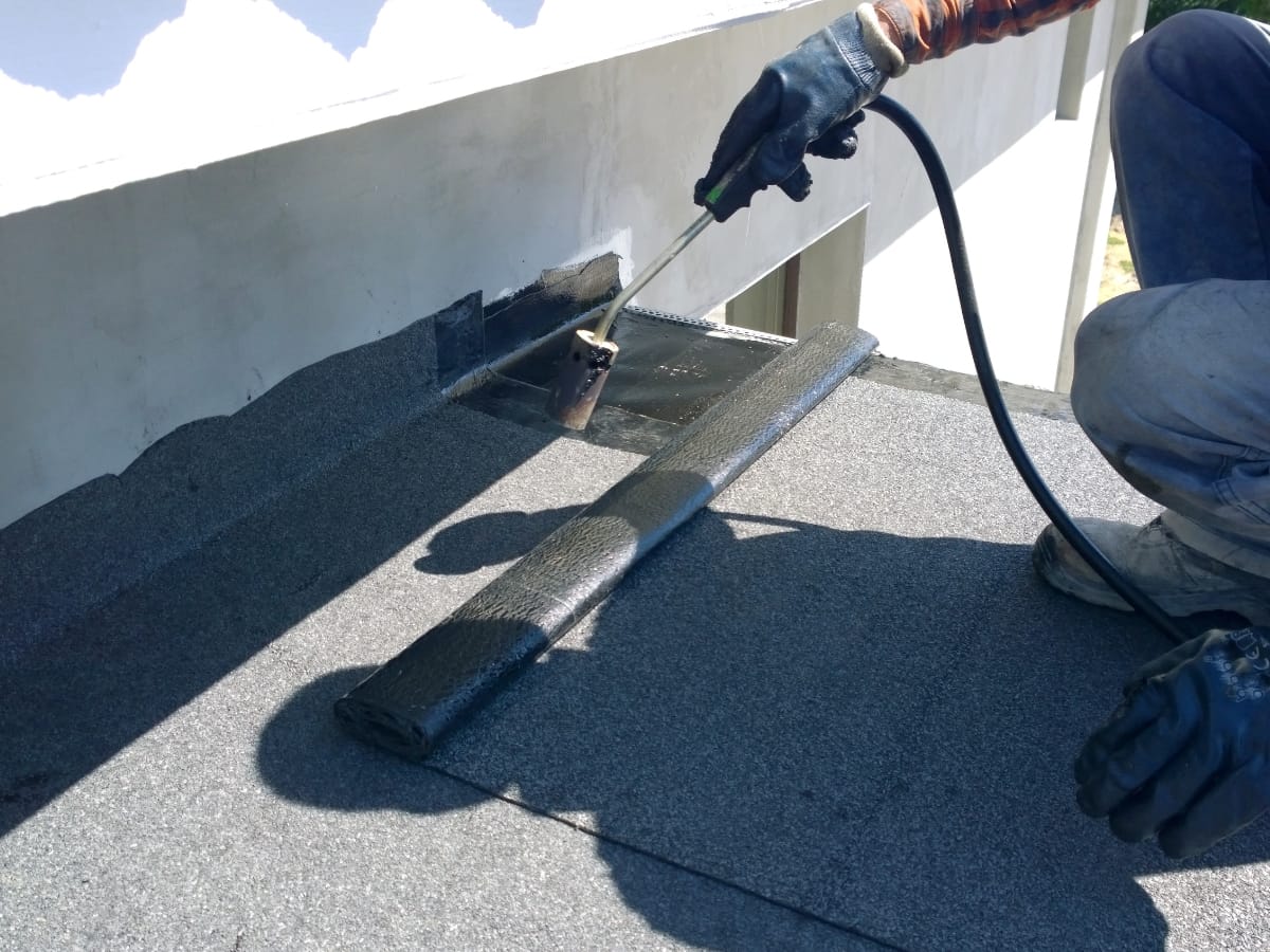 A worker expertly installs waterproof roofing material with a blowtorch on a commercial flat roof.